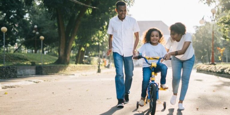 An image of parents teach their kid to ride bicycle.